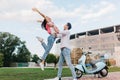 Inspired slim girl in vintage jeans jumping with hands waving while boyfriend holding her. Young people having fun on