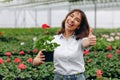 Inspired smiling young woman florist holding flowers of begonia in greenhouse. Female gardener working with plants Royalty Free Stock Photo