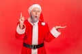 Inspired thoughtful elderly man in santa claus costume pointing finger up, has good idea about holidays celebration, solution Royalty Free Stock Photo