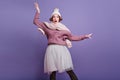 Inspired woman in funny winter hat waving hands on purple background. Indoor photo of winsome brunette girl in lush