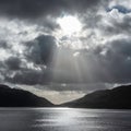 Inspiring majestic sunbeams streaming through dramatic clouds onto calm waters of Loch Lomond landscape during Winter sunset Royalty Free Stock Photo
