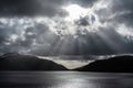 Inspiring majestic sunbeams streaming through dramatic clouds onto calm waters of Loch Lomond landscape during Winter sunset Royalty Free Stock Photo