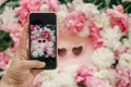 Instagram blogging concept. Hand holding phone and taking photo of stylish girly flat lay of heart shape pink sunglasses with pink