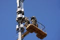 Installation of cellular equipment on the tower. Two communications engineers work at altitude from a lifting cradle. Copy space