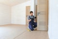 Installation of a lock on the front wooden entrance door. Portrait of young locksmith workman in blue uniform installing Royalty Free Stock Photo