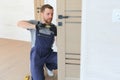 Installation of a lock on the front wooden entrance door. Portrait of young locksmith workman in blue uniform installing Royalty Free Stock Photo