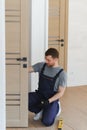 Installation of a lock on the front wooden entrance door. Portrait of young locksmith workman in blue uniform installing Royalty Free Stock Photo