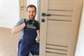 Installation of a lock on the front wooden entrance door. Portrait of young locksmith workman in blue uniform installing Royalty Free Stock Photo