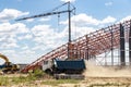 Installation of metal trusses and frame during the construction of an industrial building or factory. The dump truck removes