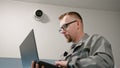 Installer in uniform sets up security camera in office room using laptop