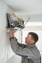 Installing air conditioner in apartment. Technician man in work uniform screwing air cooler to wall.