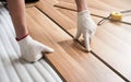 Installing laminated floor, detail on man hands in gloves fitting wooden tile, over white foam base layer, tape measure in Royalty Free Stock Photo