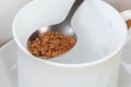 Instant coffee granules in spoon atop empty cup close-up