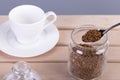 Instant coffee in a spoon.Glass transparent jar with granules.White coffee cup and saucer on a wooden surface.Overlaying ,