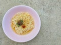 Instant noodle in a pink bowl with some seasoning ingredient