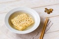 Instant noodles in white bowl, chopsticks and heap of coins on a white wooden table. Concepts of poverty, malnutrition and cheap