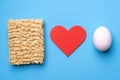 Instant noodles and white chicken egg on a blue background. A red heart between them. Instant egg noodles love Royalty Free Stock Photo