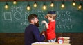 Instructive conversation concept. Child in graduate cap listening teacher, chalkboard on background, rear view. Teacher