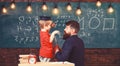 Instructive conversation concept. Child in graduate cap listening teacher, chalkboard on background, rear view. Teacher Royalty Free Stock Photo