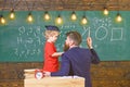 Instructive conversation concept. Teacher with beard, father teaches little son in classroom, chalkboard on background Royalty Free Stock Photo