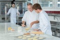 Instructor and apprentice in bakery making pretzels