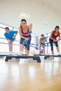 Instructor with fitness class performing step aerobics exercise with dumbbells Royalty Free Stock Photo