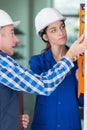Instructor with young woman with hardhat carrying water level