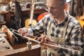 Mature instrument maker inside a rustic workshop is skillfully heating the hair of a violin bow to adjust its length. Blurred back