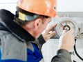 Instrumentation fitter checks and adjusts operation of pressure gauge indoors at industrial facility. Back view.