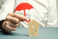 An insurance agent is holding a red umbrella over a wooden house. Property insurance concept. Protection of housing / house. Royalty Free Stock Photo