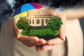 Insurance concept - umbrella demonstrating protection. Woman holding house model with green lawn Royalty Free Stock Photo