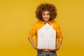 Insurance, property purchase. Joyful bright pretty woman with fluffy curly hair in hoody holding paper house