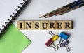 INSURER - word on wooden cubes with stationery clips, pencils, notebook