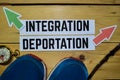 Integration or Deportation opposite direction signs with sneakers, eyeglasses and compass on wooden