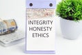 INTEGRITY HONESTY ETHICS text, word, inscription on a desktop calendar on a white background next to money and a green flower