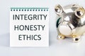 INTEGRITY HONESTY ETHICS A word, a text written on a white sheet next to a piggy bank Royalty Free Stock Photo