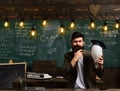 Intellectual task concept. Bearded hipster with bulb and chalkboard on background. Guy thinking with thoughtful