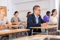 Intelligent adult man in glasses listening to lecture in classroom