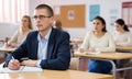 Intelligent adult man in glasses listening to lecture in classroom