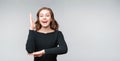 Intelligent enthusiastic young woman raises her hand up to attract attention and answer a question. Gray background