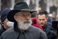 An intelligent gray-haired aged man in eye-glasses with a beard and mustache in a black wide-brimmed hat and gray coat in the