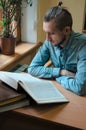 Intelligent male hipster student reading book and sitting at the table in public university library. Side view shot of Royalty Free Stock Photo