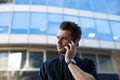 Intelligent man manager talking via cellphone while standing outdoors business centre. Royalty Free Stock Photo