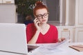 Intelligent prosperous young businesswoman dressed casually, has ginger knot, studies documentation and consults executive directo