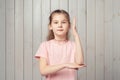 Intelligent teen girl in pink t shirt raises her hand up with a happy smile to attract attention and answer a question