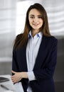 Intelligent young business woman in a blue jacket is standing at her workplace. Portrait of a specialist in a modern
