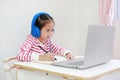 Intend asian little child girl writing and using headphone study online learning class with laptop computer during new normal