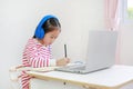 Intend asian little child girl writing and using headphone study online learning class with laptop computer during new normal