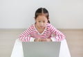 Intend asian little child sitting at desk and using laptop at home