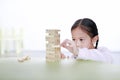 Intend little Asian child girl thinking to playing wood blocks tower game for Brain and Physical development skill in a classroom